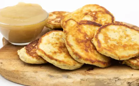 Goldbraune Quarkkeulchen ohne Kartoffeln, serviert mit Apfelmus auf einem Holzbrett.