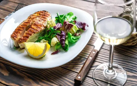 Gegrilltes Lachsfilet mit Salat und Zitrone, dazu ein Glas Weißwein, der den Riesling Geschmack unterstreicht.