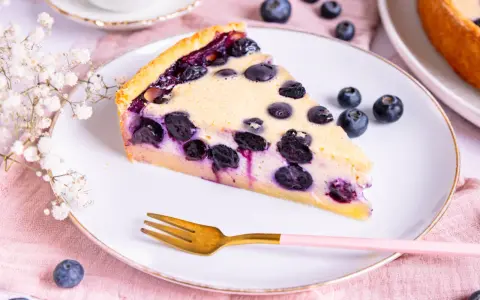 Ein Stück saftiger Heidelbeerkuchen Landfrauenart auf einem Teller, garniert mit frischen Beeren und einer Gabel.