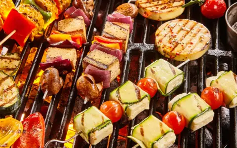 Bunte Spieße mit Tofu, Zucchini, Tomaten und Mais werden auf einem Grill zubereitet. Ein Genuss für vegetarisches Grillen!