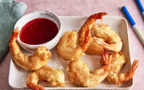 Knusprige tempura garnelen auf einem Teller mit süß-saurer Sauce und Stäbchen.