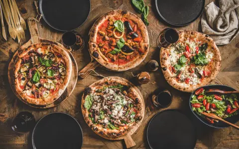 Vier leckere Pizzen und ein Salat auf Holztisch. Die Frage welcher Wein zu Pizza passt, wird hier mit Rotwein beantwortet.