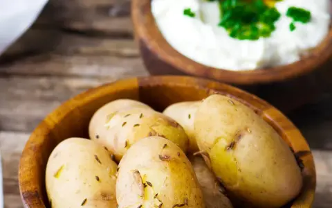 Kleine, gekochte Kartoffeln mit Kümmel in einer Holzschale, daneben eine Schale mit Quark und Kräutern. Ein rustikales Gericht: Kartoffeln mit Quark.