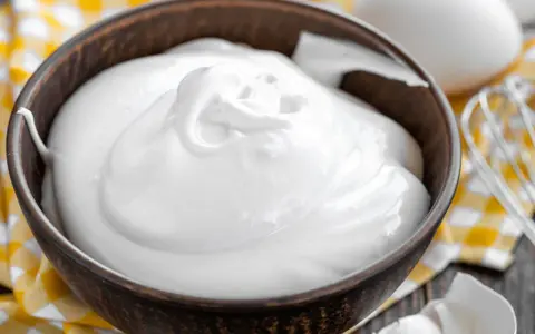 Perfekt geschlagener Eischnee in einer Schüssel, bereit für süße Kreationen. Daneben liegen Eier und ein Schneebesen.