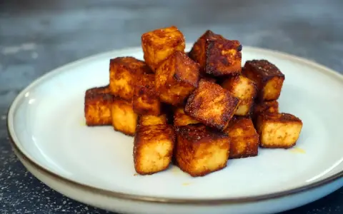 Goldbraun gebratene Tofuwürfel, perfekt zum tofu zubereiten. Knusprig und lecker auf einem Teller angerichtet.