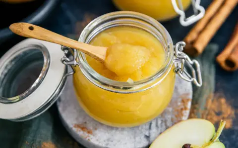 Frisch zubereitetes Apfelmus selber machen ist einfach! Ein Glas voller hausgemachtem Apfelmus, mit einem Holzlöffel und Zimtstangen.