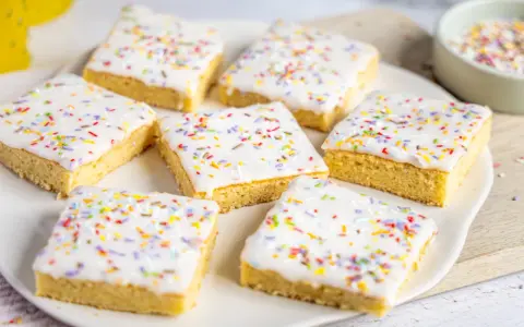 Sieben quadratische Kuchenstücke mit weißer Glasur und bunten Streuseln, perfekt für ein schnelles Fantakuchen Tassenrezept.