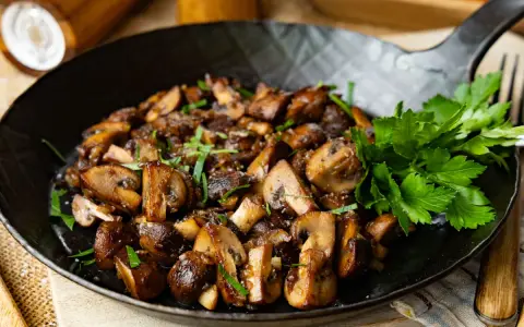 Gebratene Champignons in einer Pfanne, garniert mit frischer Petersilie. Köstlich und einfach zuzubereiten.