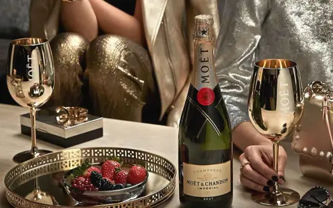Elegante Szene mit Moët & Chandon Champagnerflasche, goldenen Gläsern und Beeren. Die Herkunft des Luxus wird durch die Marke und die festliche Atmosphäre betont.
