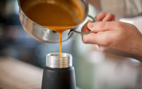 Eine orangefarbene Flüssigkeit wird aus einem Topf in ein schwarzes Gefäß gegossen. Ist das eine Espuma?
