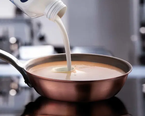 Sahne wird in eine Pfanne mit einer cremigen Sauce gegossen. Perfekt, welche Sahne zum Kochen für eine köstliche Mahlzeit.