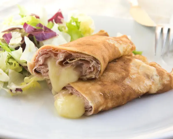 Herzhafte Pfannkuchen gefüllt mit Schinken und geschmolzenem Käse, serviert mit einem frischen Salat.