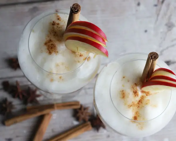 Zwei cremige Wintercocktails mit Zimt, Apfelscheiben und Sternanis.