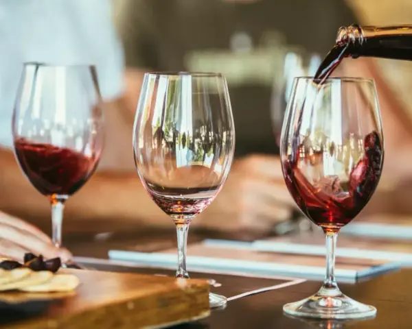 Rotwein wird in ein Glas gegossen, der Duft von **Wein** und **Tanninen** liegt in der Luft. Daneben ein leeres Glas und ein Teller mit Käse und Crackern.