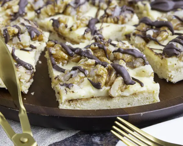Ein "friss dich dumm kuchen" mit cremiger Füllung, Walnüssen und Schokoladendrizzle auf einem Holztablett. Goldene Gabeln liegen bereit.