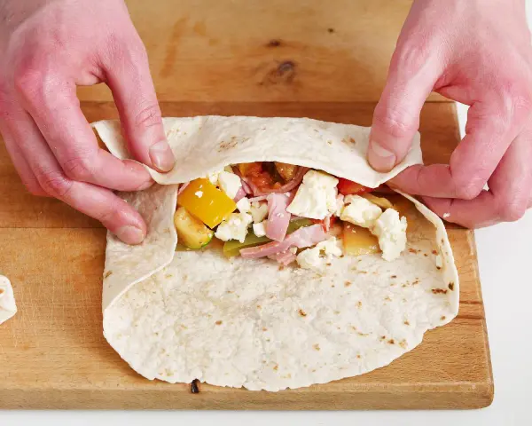 Hände falten wraps mit Gemüse, Schinken und Käse.