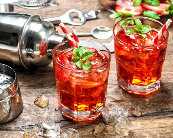 Zwei erfrischende Cocktails mit Erdbeeren und Minze, bereit zum Genießen. Dazu ein Shaker und Eiswürfel auf Holztisch. Perfekt für gute Cocktails.