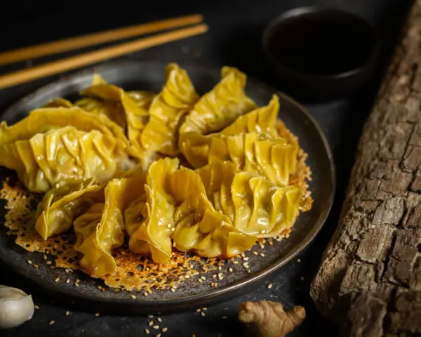 Goldbraune Gyoza auf knusprigem Sesam-Bett, bereit für ein köstliches Dumplings-Rezept. Dazu Sojasauce und Ingwer.