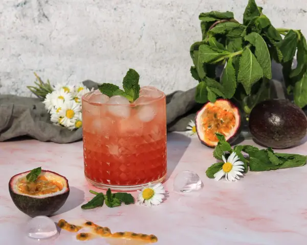 Erfrischender sanbitter cocktail mit Passionsfrucht, Minze und Eiswürfeln, garniert mit Gänseblümchen.