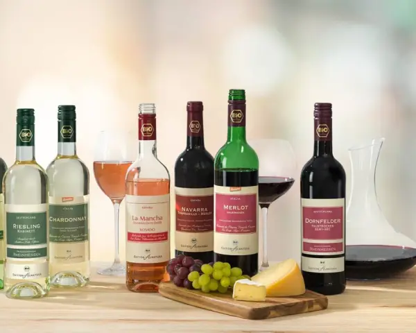 Eine Auswahl an Bio-Weinen, darunter verschiedene Weißwein Sorten wie Riesling und Chardonnay, neben Rot- und Roséweinen, Käse und Trauben.
