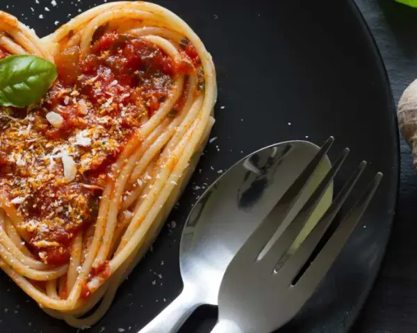 Herzförmige Spaghetti mit Tomatensoße und Basilikum, ein liebevolles Gericht für Pasta Rezepte. Daneben liegen Knoblauch und Tomaten.
