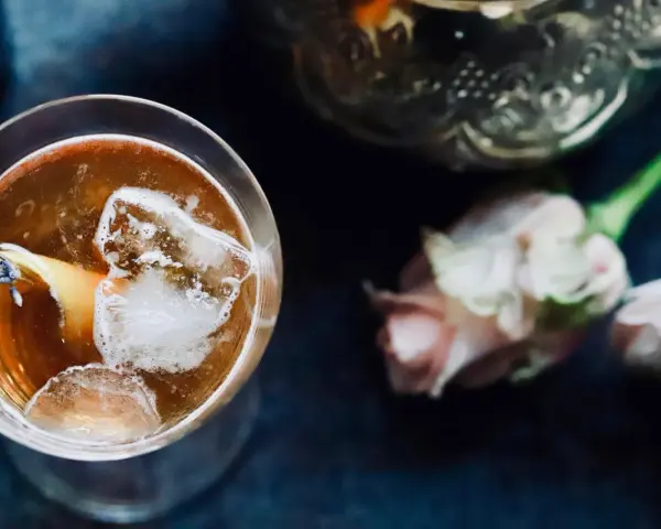 Ein erfrischender Gin Tee mit Eis, Zitrone und Lavendelblüten. Daneben zarte Rosen und eine verzierte Karaffe.