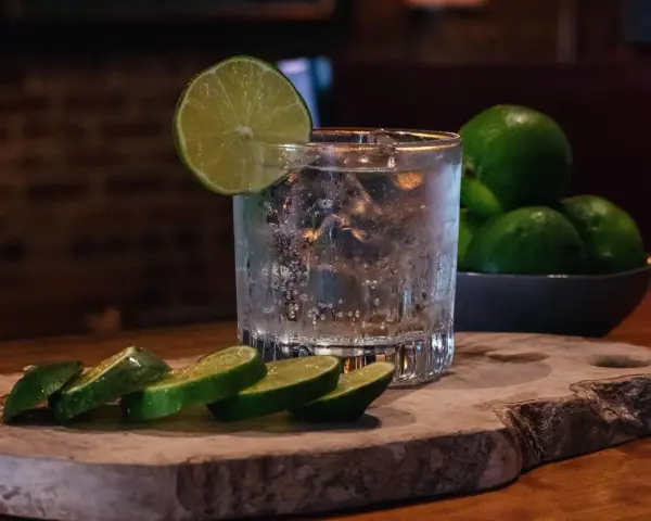 Ein erfrischender Gin Tonic, der klassische Cocktail, mit Eis, Limettenscheiben und frischen Limetten im Hintergrund.