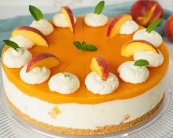 Eine Maracuja Torte mit Pfirsichstücken und Sahnetupfern, verziert mit Minze.