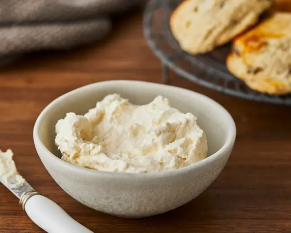 Cremiger Aufstrich in einer Schale, bereit für das perfekte Scones Rezept. Daneben ein Messer mit etwas Aufstrich.
