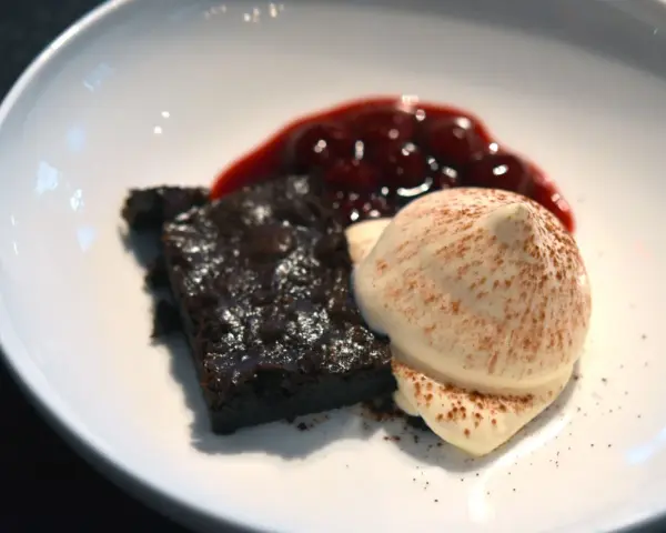Schokoladenbrownie mit Fruchtsauce und einer perfekt hergestellten, luftigen Espuma, bestäubt mit Kakao.