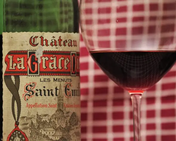 Ein Glas Rotwein neben einer Flasche Château La Grace Dieu. Die Bedeutung von "Grand Cru" auf dem Etikett deutet auf höchste Qualität hin.