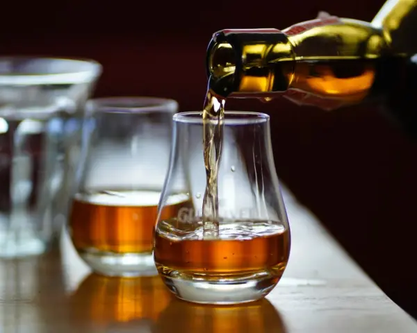 Bernsteinfarbener schottischer Whisky fließt aus einer Flasche in ein Glas. Die schottischer Whisky sorten alphabetisch zu verkosten ist ein Genuss.