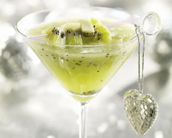Erfrischender Kiwi-Cocktail im Martiniglas, garniert mit frischen Kiwischeiben und einem glitzernden Herz-Anhänger.