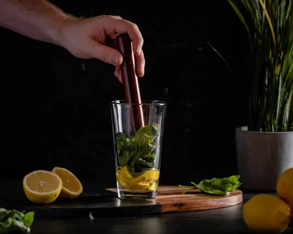 Ein Barkeeper bereitet einen erfrischenden Cocktail mit Basilikum und Gin zu, indem er die Zutaten im Glas zerdrückt.