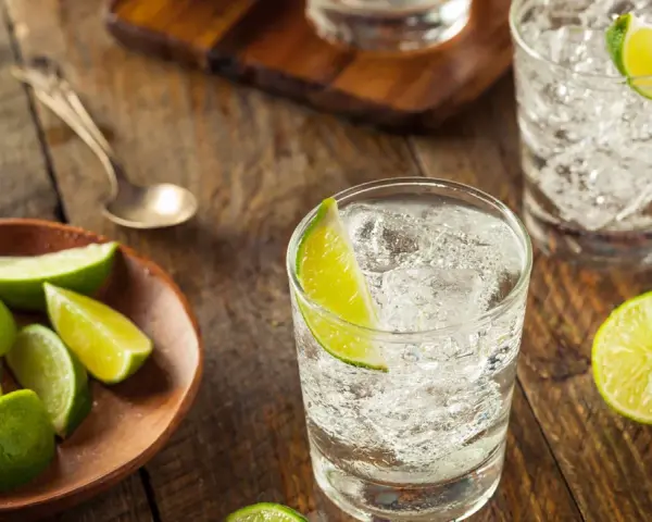 Erfrischender Jean Tonic mit Eis und Limettenspalten auf rustikalem Holztisch.