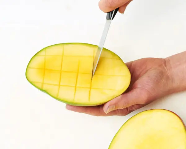 Eine Hand schneidet mit einem Messer eine reife Mango in Würfel. So einfach lässt sich die Frucht für den Verzehr vorbereiten.