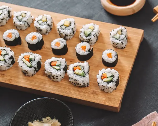 Selbstgemachtes Sushi mit Karotten und Gurken auf einem Holzbrett. So einfach kann Sushi selber machen sein!