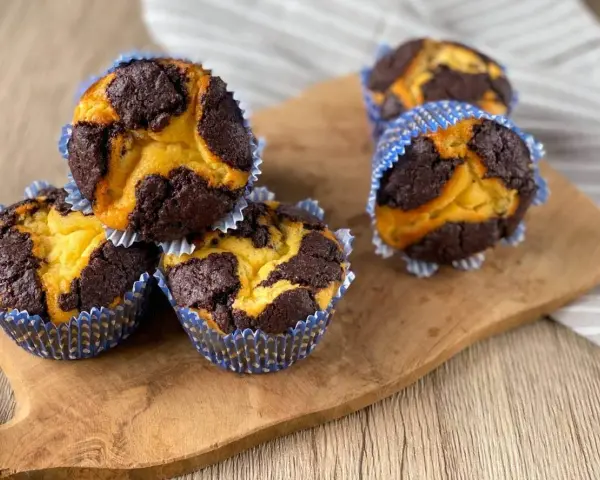 Zupfkuchen Muffins mit Marmormuster aus dunklem Schoko- und hellem Teig in blauen Papierförmchen auf einem Holzbrett.