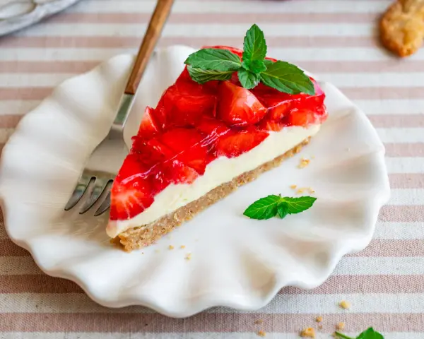 Ein Stück einfache Torte mit Erdbeeren und Minze auf einem weißen Teller.