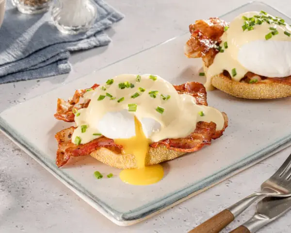 Zwei köstliche Eggs Benedict auf einem Teller, mit flüssigem Eigelb und garniert mit Schnittlauch.