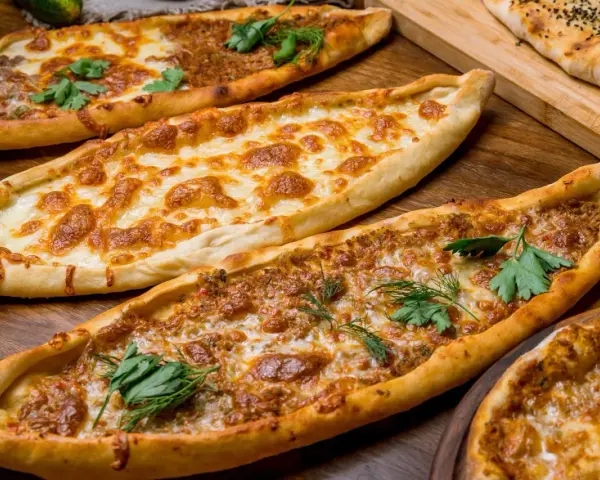 Mehrere Pide-Gerichte, darunter eines mit Käse und eines mit Hackfleisch, sind auf einem Holztisch arrangiert. Ein köstliches Pide Rezept!