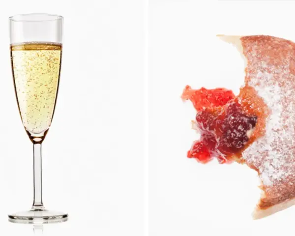 Sektglas mit Bläschen und ein angebissener Krapfen mit Marmelade. Wein Kalorien sind oft unterschätzt.