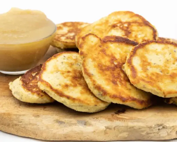 Goldbraune Quarkkeulchen ohne Kartoffeln, serviert mit Apfelmus auf einem Holzbrett.