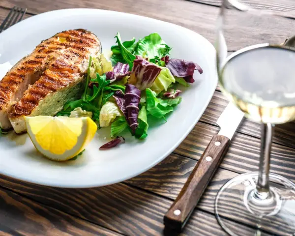 Gegrilltes Lachsfilet mit Salat und Zitrone, dazu ein Glas Weißwein, der den Riesling Geschmack unterstreicht.