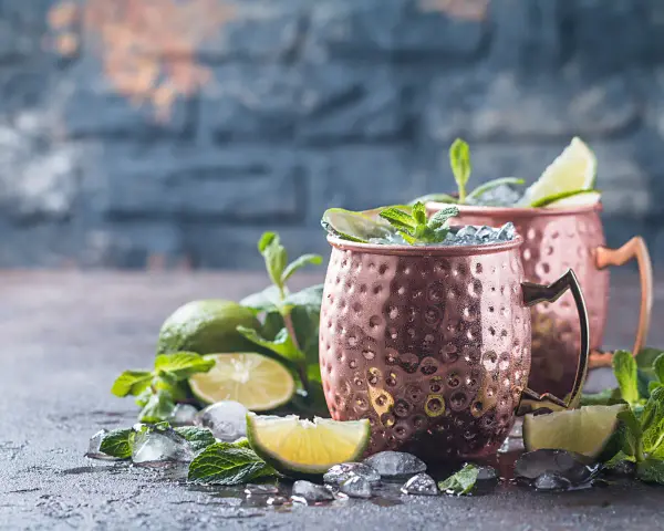 Zwei eisgekühlte Kupferbecher mit einem erfrischenden alkoholfreien Ginger Beer Cocktail, garniert mit Limette und Minze.