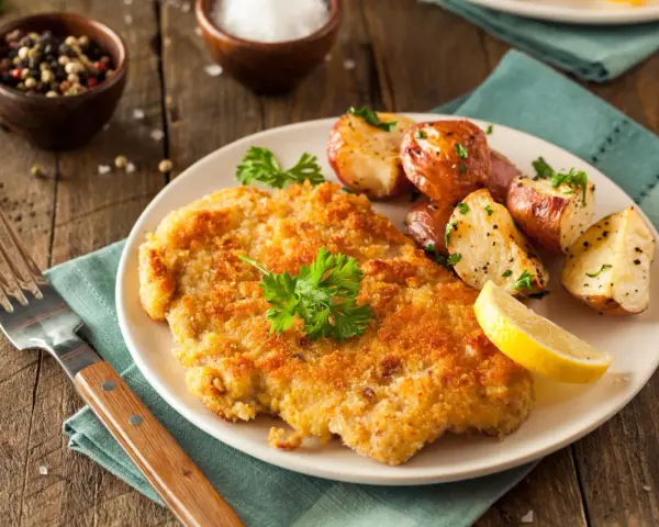 Goldbraunes Schnitzel, perfekt paniert, mit Rosmarinkartoffeln und Zitrone. Die richtige **Schnitzel panieren Reihenfolge** macht's möglich!