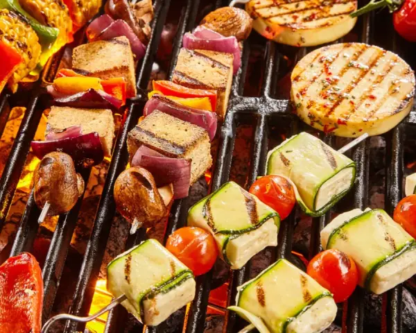 Bunte Spieße mit Tofu, Zucchini, Tomaten und Mais werden auf einem Grill zubereitet. Ein Genuss für vegetarisches Grillen!