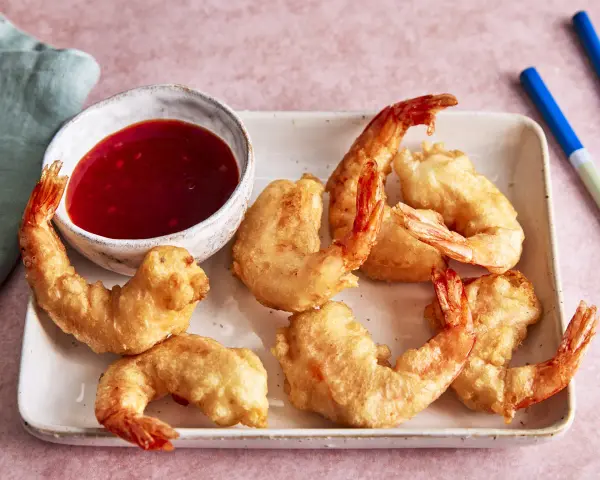 Knusprige tempura garnelen auf einem Teller mit süß-saurer Sauce und Stäbchen.