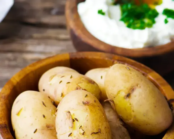 Kleine, gekochte Kartoffeln mit Kümmel in einer Holzschale, daneben eine Schale mit Quark und Kräutern. Ein rustikales Gericht: Kartoffeln mit Quark.