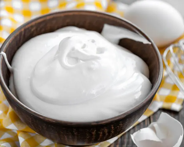 Perfekt geschlagener Eischnee in einer Schüssel, bereit für süße Kreationen. Daneben liegen Eier und ein Schneebesen.